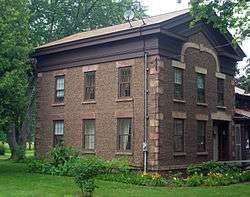 A two-story brown house made of small stones in rows. There are two small satellite dishes on top.