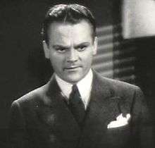 Head and shoulders shot of Cagney, looking stern, wearing a suit with a white handkerchief in his pocket.