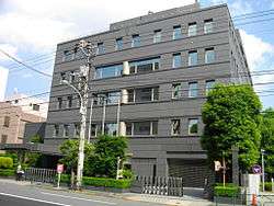 five-story building fronted by trees, hedges and city street