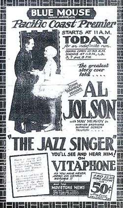 Advertisement from the Blue Mouse Theater announcing the Pacific Coast premiere of The Jazz Singer, billed as "The greatest story ever told". A photo of stars Al Jolson and May McAvoy accompanies extensive promotional text, including the catchphrase "You'll see and hear him on Vitaphone as you've never seen or heard before". At the bottom is an announcement of an accompanying newsreel.