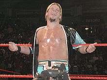 A color photograph of a Caucasian wrestler smiling as he leans back against the ropes.