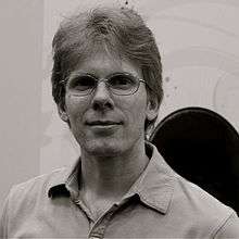 Black and white photo of the head and shoulders of a man wearing glasses