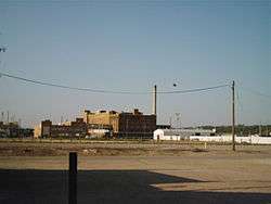 Fuzzy photo of five- or six-story brick building with a single tall smokestack