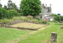 Low stone walls in grass, surrounded by trees with a house in the dissolvedtance.