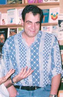 Smiling man dressed in blue, standing in front of books