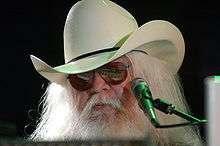 Musician Leon Russell is shown from the head up in front of a microphone.