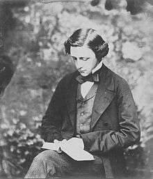 Photographic portrait of Charles Lutwidge Dodgson (Lewis Carroll), seated and holding a book