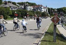 Bicyclists on a road. Houses can be seen at left.