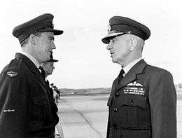 Informal half portrait of two men wearing dark military uniforms with peaked caps, in conversation outdoors