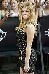 A young woman with long blonde hair, in a short black dress in front of spectators with cameras.