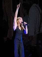 Madonna singing into a microphone in her left hand, while pointing her right hand upwards.