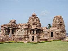 Two stone temples against blue sky, behind grassy area