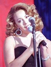 A woman wearing a dress is facing left and holding a microphone.