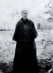 A grey haired woman wearing all black, standing outdoors.