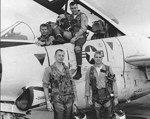 Four military pilots posed in, on, or in front of, silver jet with United States markings