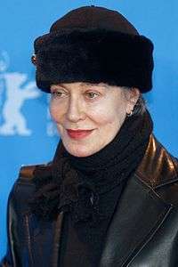 A woman in her sixties is seen wearing a leather jacket and a black hat.