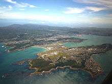 A sprawling city on a peninsula as seen from an aircraft. The landmass is pocketed with many bays and coves.