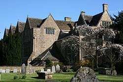 Old mansion house with traingular roofs. In the foreground is a graden with gravestones.