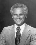 Black-and-white photo of a man with a wide smile and short curly hair wearing a light-colored suit