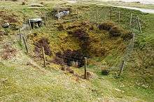 A deep pit surrounded by a unsubstantial-looking wire fence