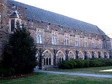 A Gothic-style exterior showcases Cathedral-like windows with intricate framework and dark, colorful stone, with bushes and grass in the foreground