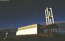 A white concrete church with a skeletal bell tower and thickly leaded stained glass.