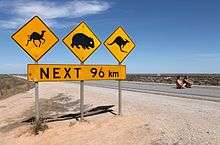 Warning signs stand out as the only feature alongside a road through a flat, treeless, landscape