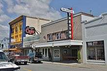 A two-story building with a painted marquee and vertical sign reading "Olympic Theatre".