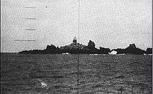 Large multiple rock outcroppings located in the middle of the ocean with a lighthouse located in the center as seen through a submarine periscope.