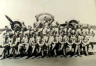 Military personnel standing or seated in front of twin-engined military monoplane