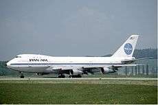 Side view of aircraft on taxiway. Grassy surfaces in foreground; hills and sky in background.