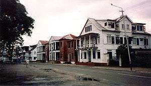 Street with two storied wooden houses. Many of the houses have a balcony along the street side.