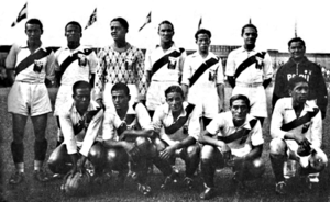 Photo of twelve men, seven standing and five crouching, inside a stadium