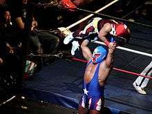 Color photo of a masked wrestler lifting a smaller masked wrestler over his head.