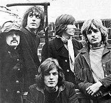 A black and white photo of five men standing in front of a brick wall.