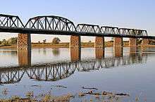 Four truss sections of a railway bridge, supported by stone pillars.