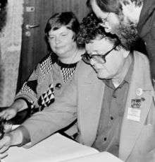 Black and white photograph of a man, in the foreground, sitting at a table.