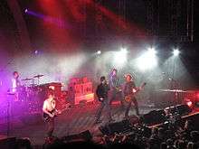 Powderfinger are on stage, with Coghill at left on drums, then Middleton on guitar, Fanning mid-stage singing into a microphone, Collins on his bass guitar and Haug at extreme right.