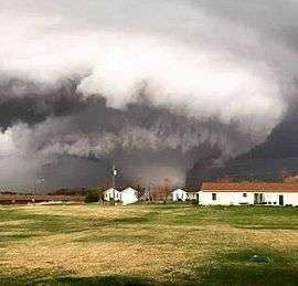 A photograph depicting a large, violent tornado; houses are evident in the foregound