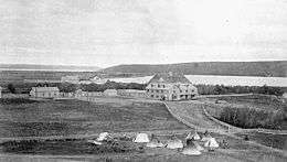 Exterior view of Qu'Appelle Indian Industrial School in Lebret, District of Assiniboia, ca. 1885. Surround land and tents are visible in the foreground.