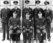 A group portrait of military officers in formal uniform. Five men are standing side-by-side in the back, while three are sitting down at the front.