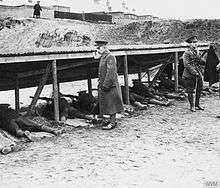 Soldiers lie down practising on a rifle range, supervised by standing colleagues.