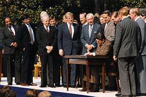 Rangel and about fourteen other men standing around a table, where President Ronald Reagan signs a bill