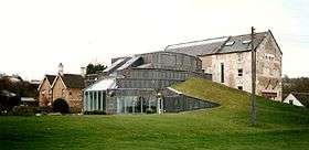 A large glass conservatory is shown attached to a house in a field.