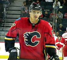 A player stares into the distance. He is wearing a red uniform with black and yellow trim and a stylized black C on his chest.