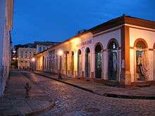 A cobblestone street of old single-storied brightly colored houses.