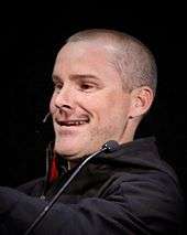 Young, smiling man in black with two microphones