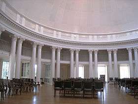 A red brick, Neoclassical dome with a large portico on the front and covered walkway on the sides lit up at dusk. Dark trees border the building on both sides.