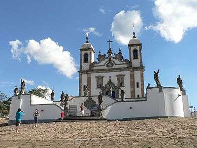 Stairs leading to a white stone church with two towers. Sculptures are placed on walls in front of the church.