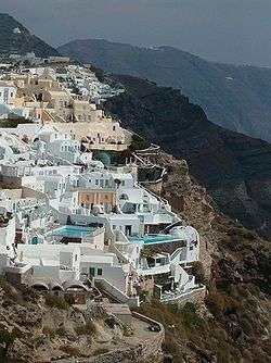 Enclave of structures built into the side of a steep cliff. Swimming pools are visible.